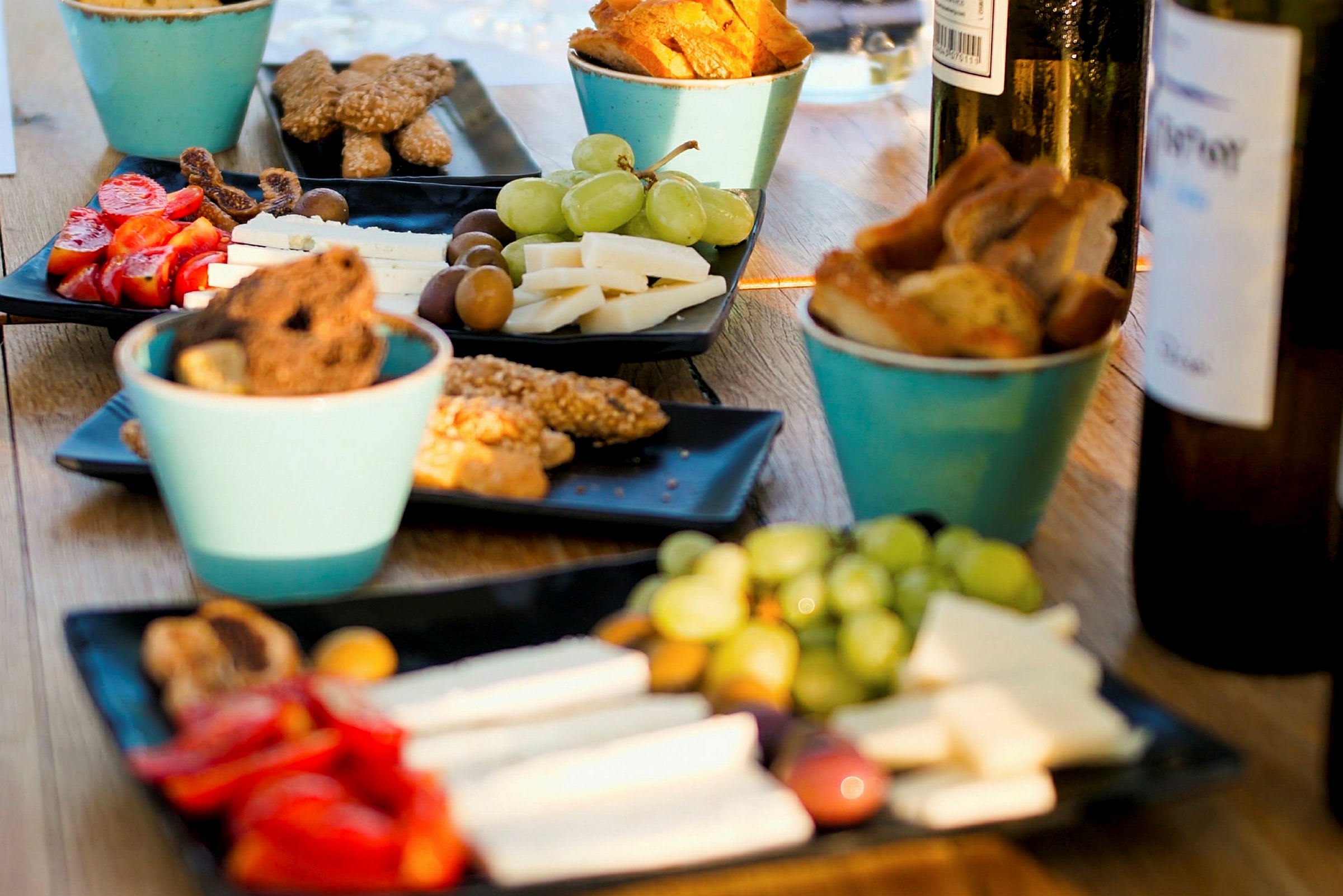 Flere tallerkener inneholder snacks som ost, grønnsaker, oliven og brød, sammen med drikkeflasker på et bord. (AI-generert tekst)