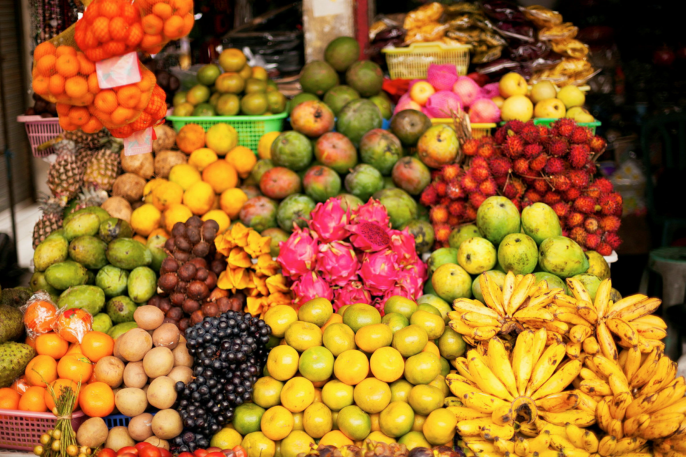 En fargerik utstilling av forskjellige frukter som mango, bananer, dragefrukt og andre på et fruktmarked. (AI-generert tekst)