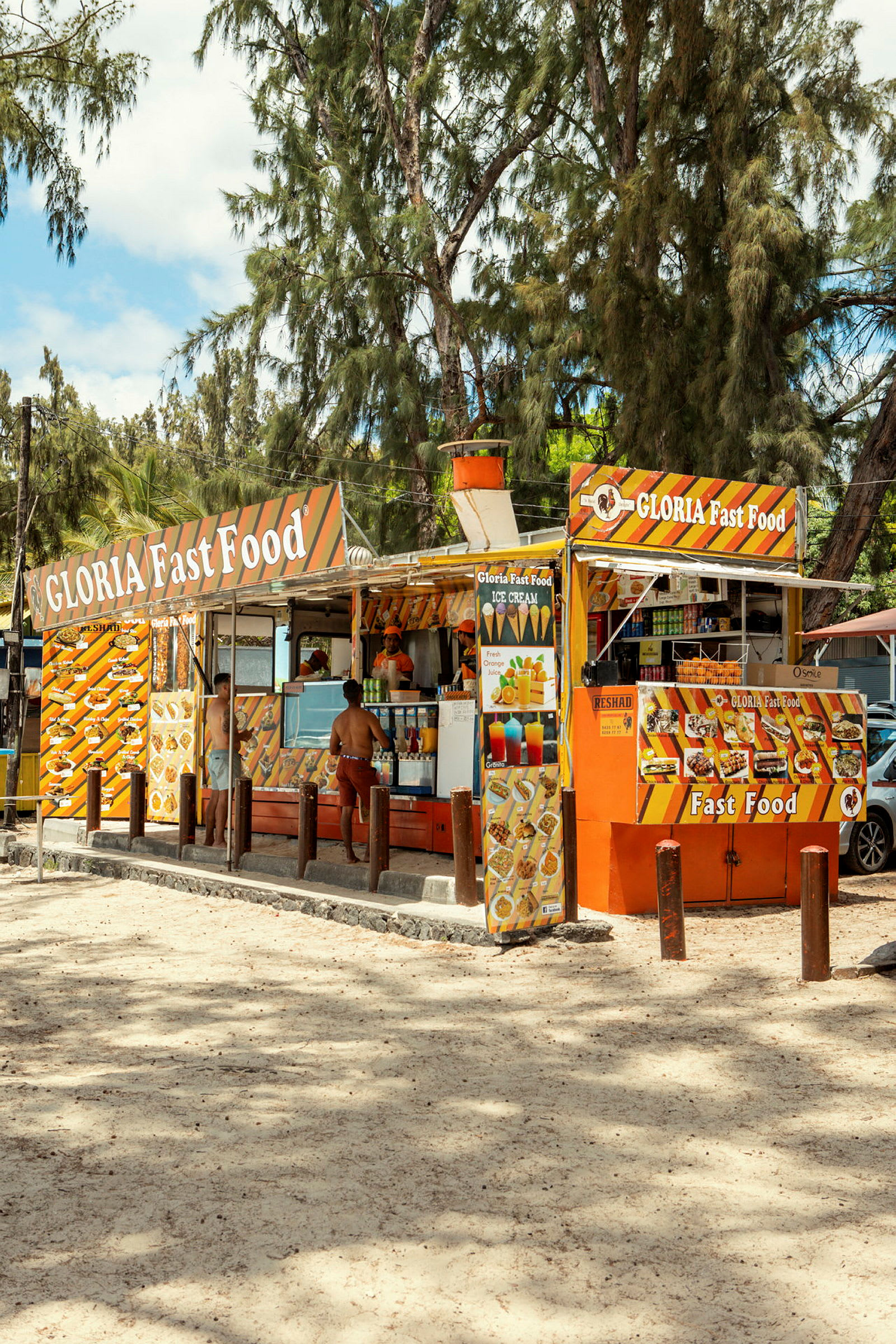 En fastfood-kiosk med oransje og gule dekorative skilt, omgitt av trær. (AI-generert tekst)