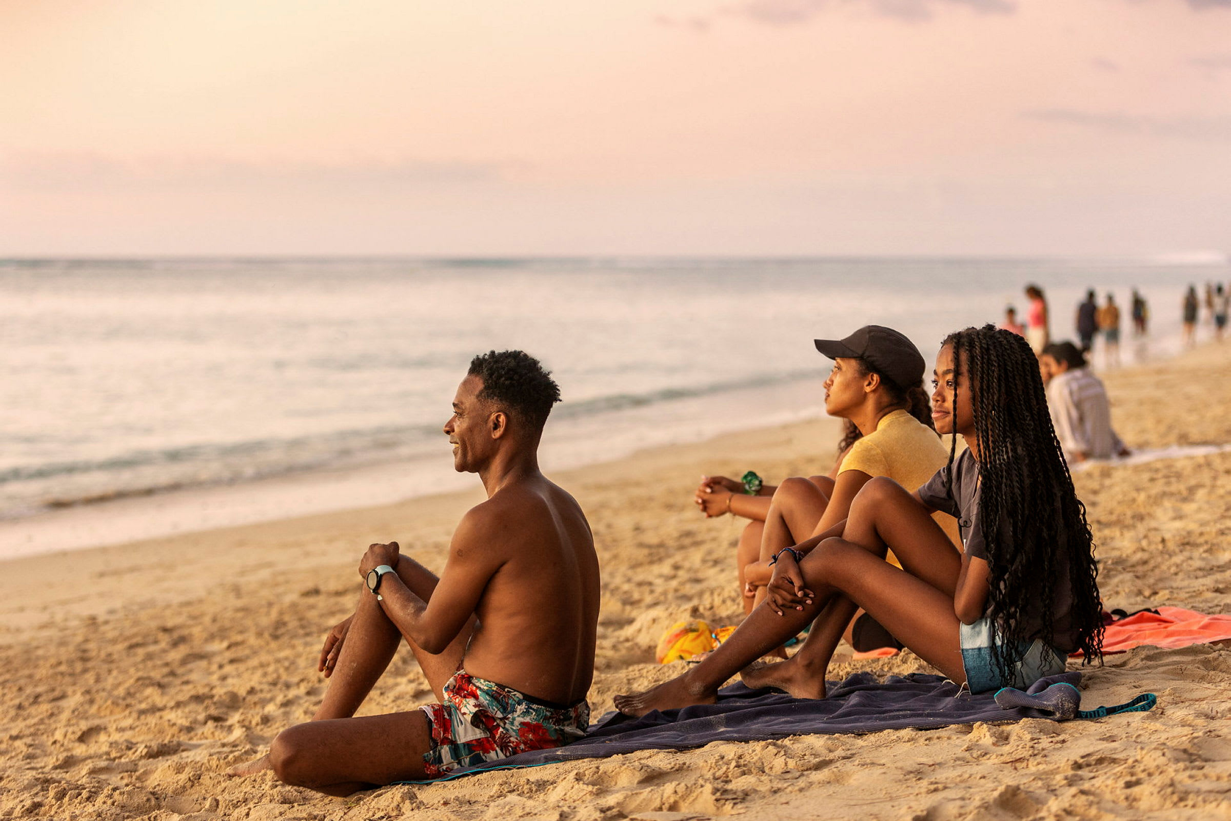 Personer sitter på en strand og ser mot havet. (AI-generert tekst)