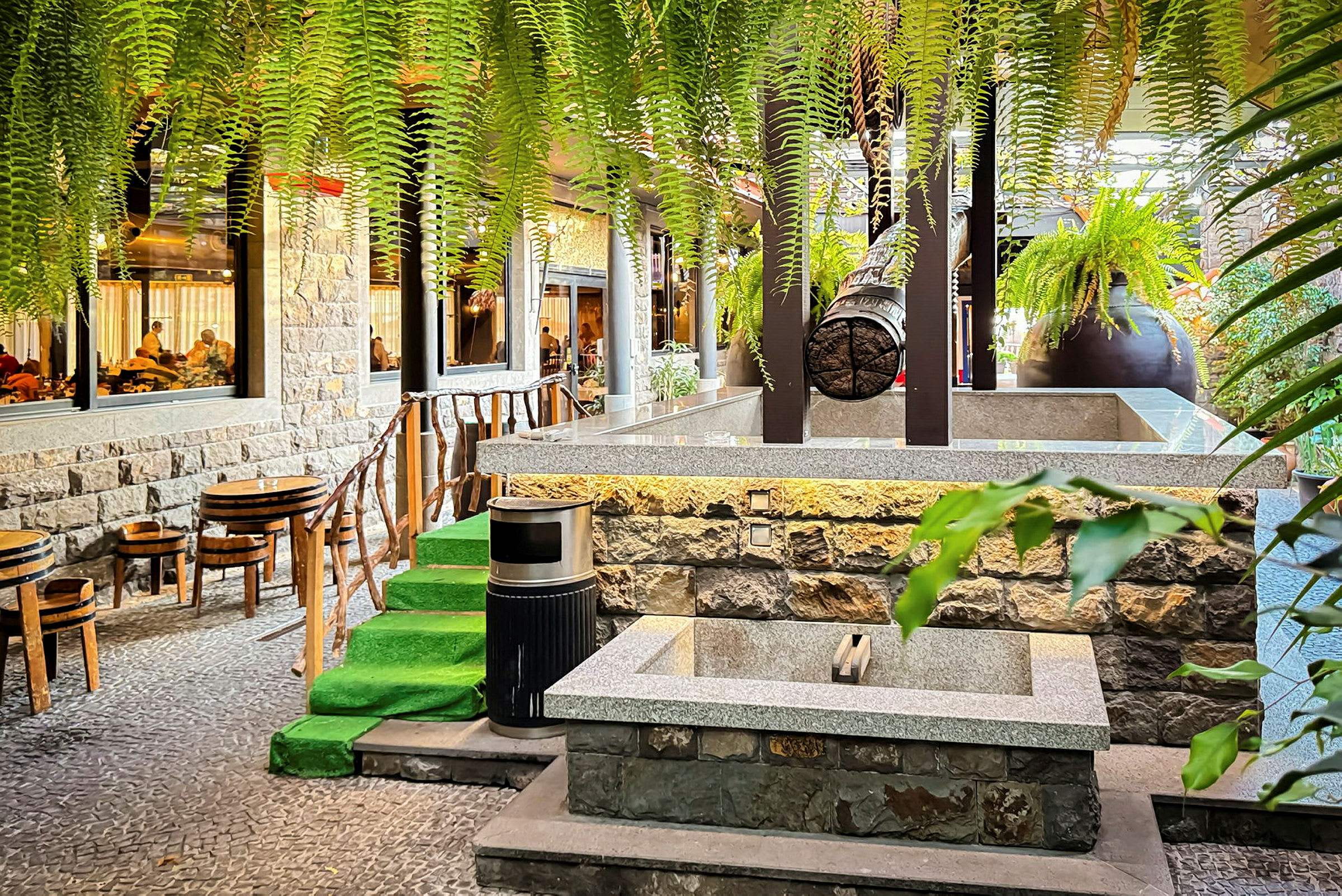 Et bilde som viser et utendørsmiljø ved en restaurant med stoler, bord, grønne planter og steintrapp. (AI-generert tekst)