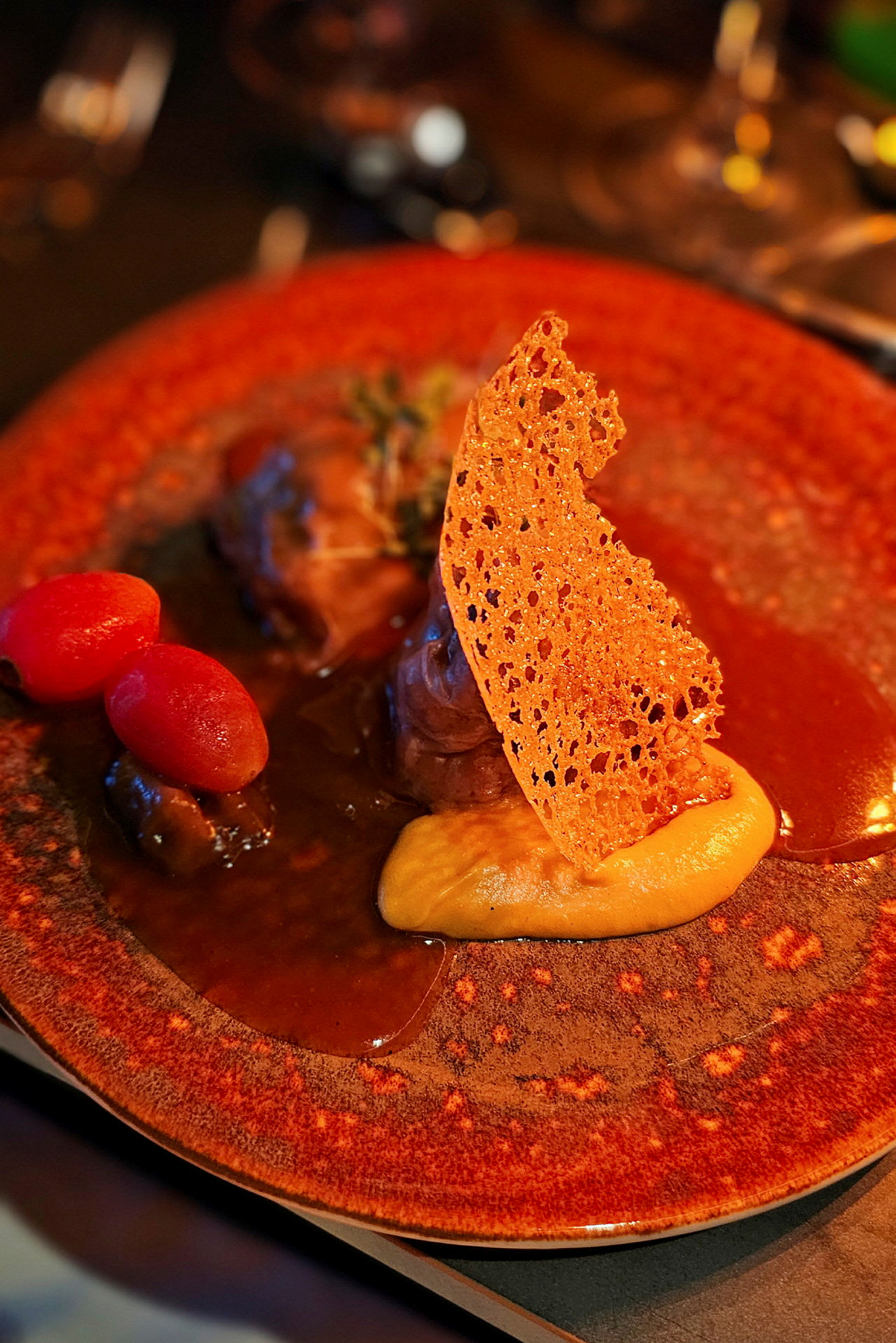 En tallerken med et gourmetmåltid anrett med saus, puré, sprø dekorasjonselement og små tomater. (AI-generert tekst)