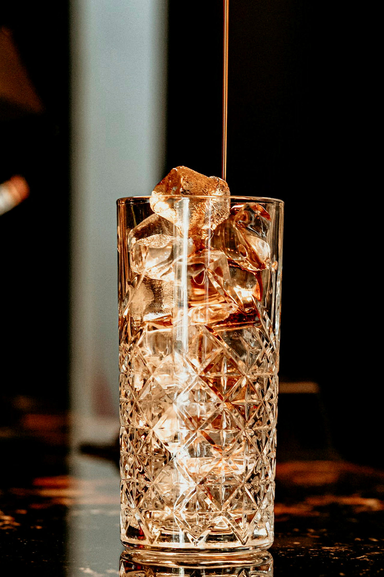 Et høyt glass med isbiter og væske som helles i. (AI-generert tekst)