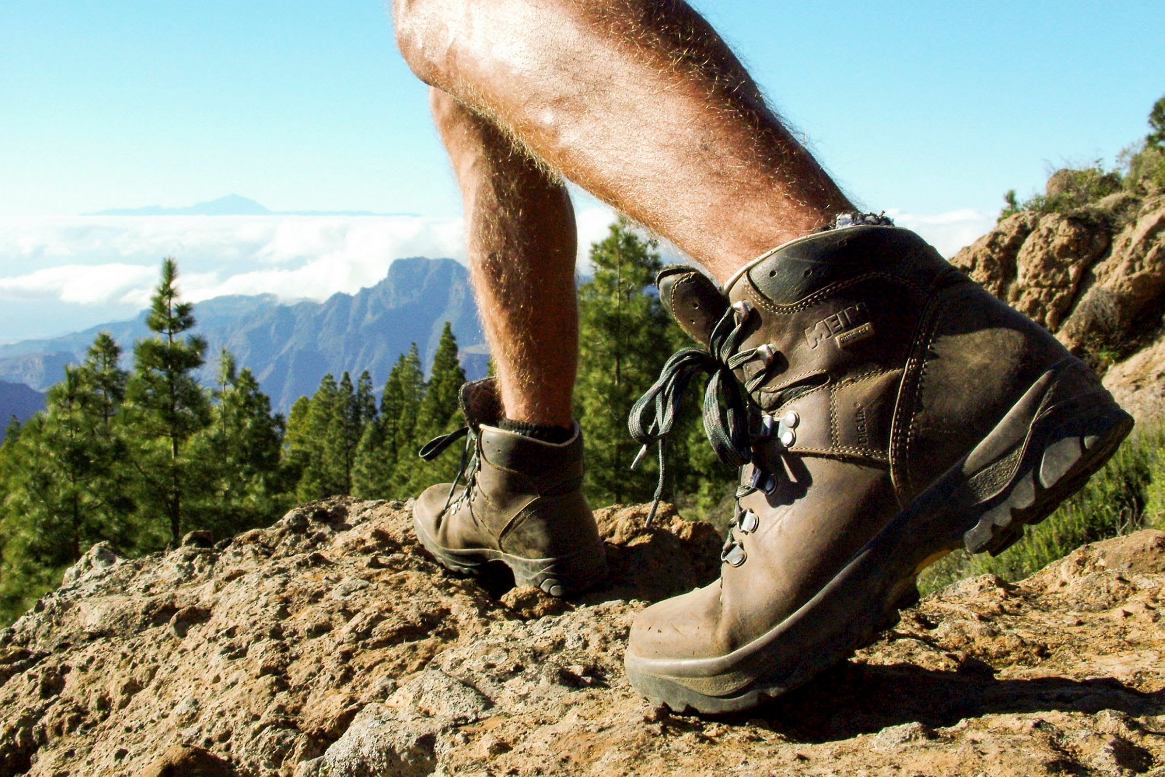 Et par fjellsko bæres av en person på en klippe med utsikt over fjell og skog. (AI-generert tekst)