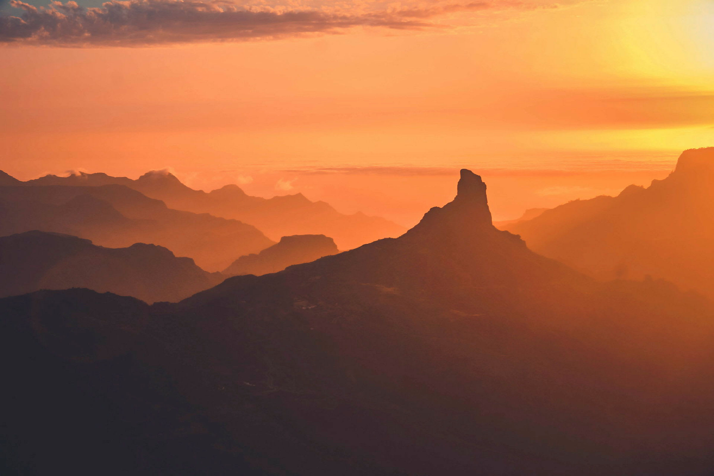 En fjelltopp vises som en silhuett mot en oransje og gul solnedgang. (AI-generert tekst)