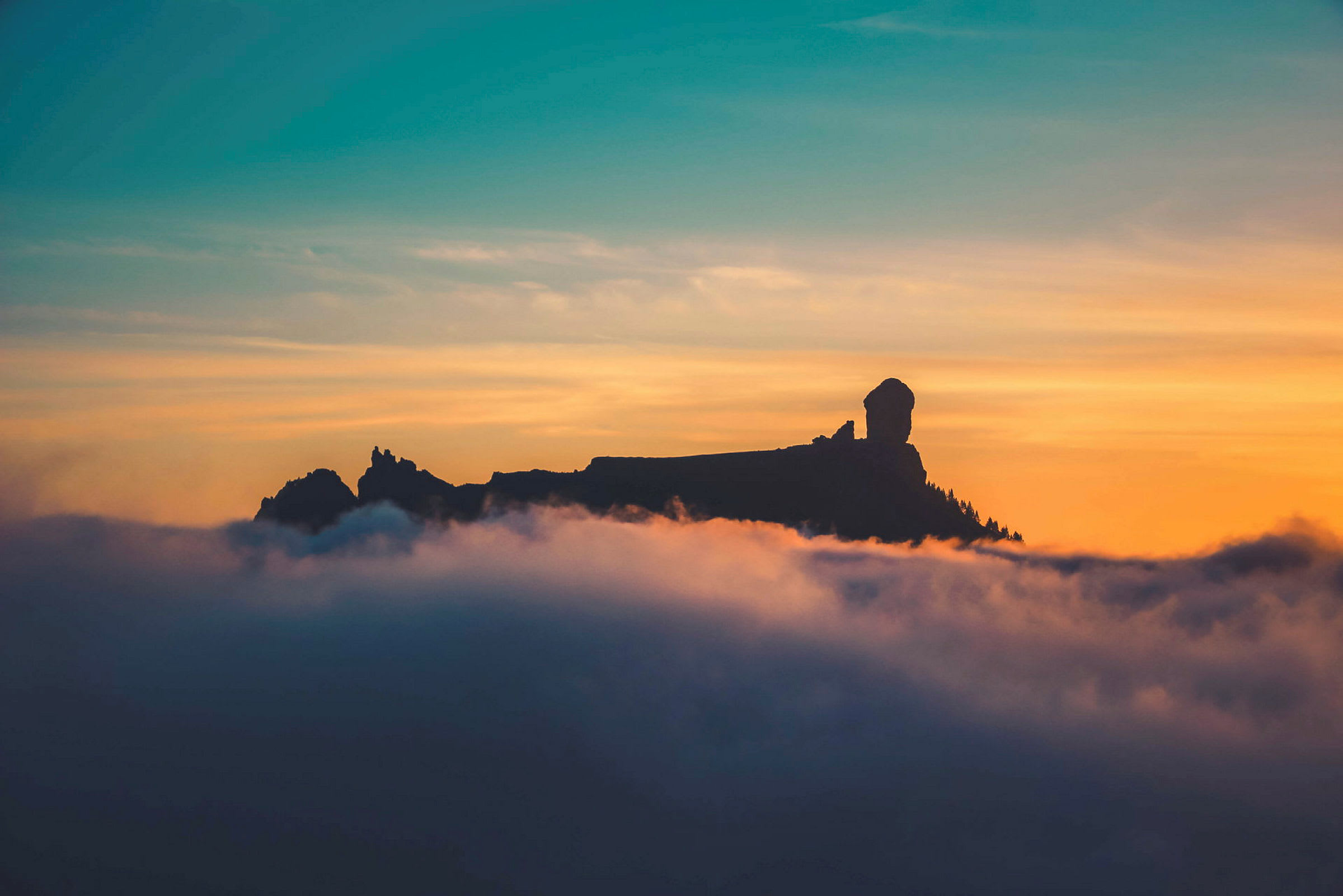 Silhuetten av en fjelltopp omgitt av skyer ved solnedgang. (AI-generert tekst)