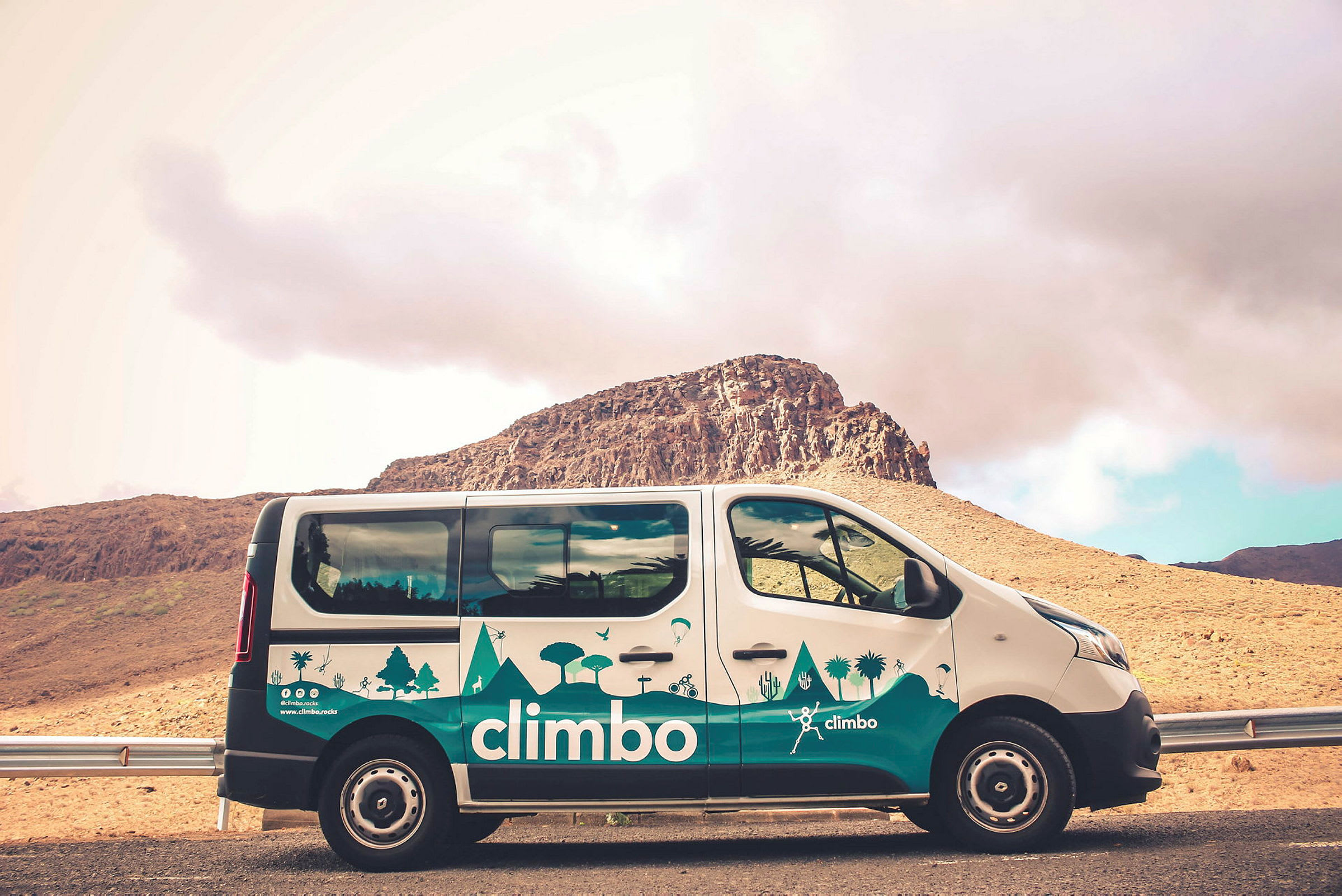 En bil med teksten 'climbo' parkert foran en fjellrik bakgrunn. (AI-generert tekst)