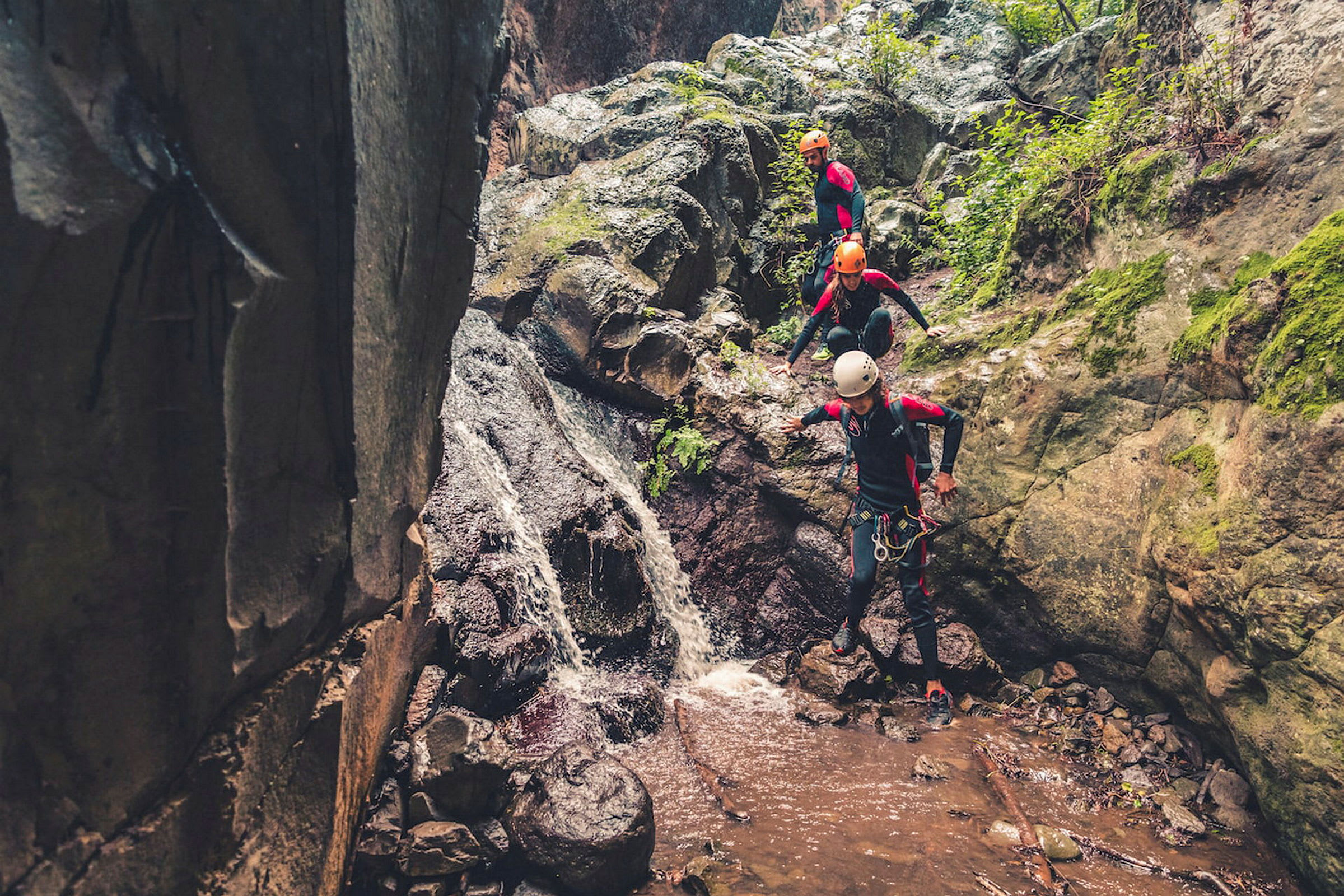 Tre personer i klatreutstyr følger en vannstrøm i en steinete ravine. (AI-generert tekst)