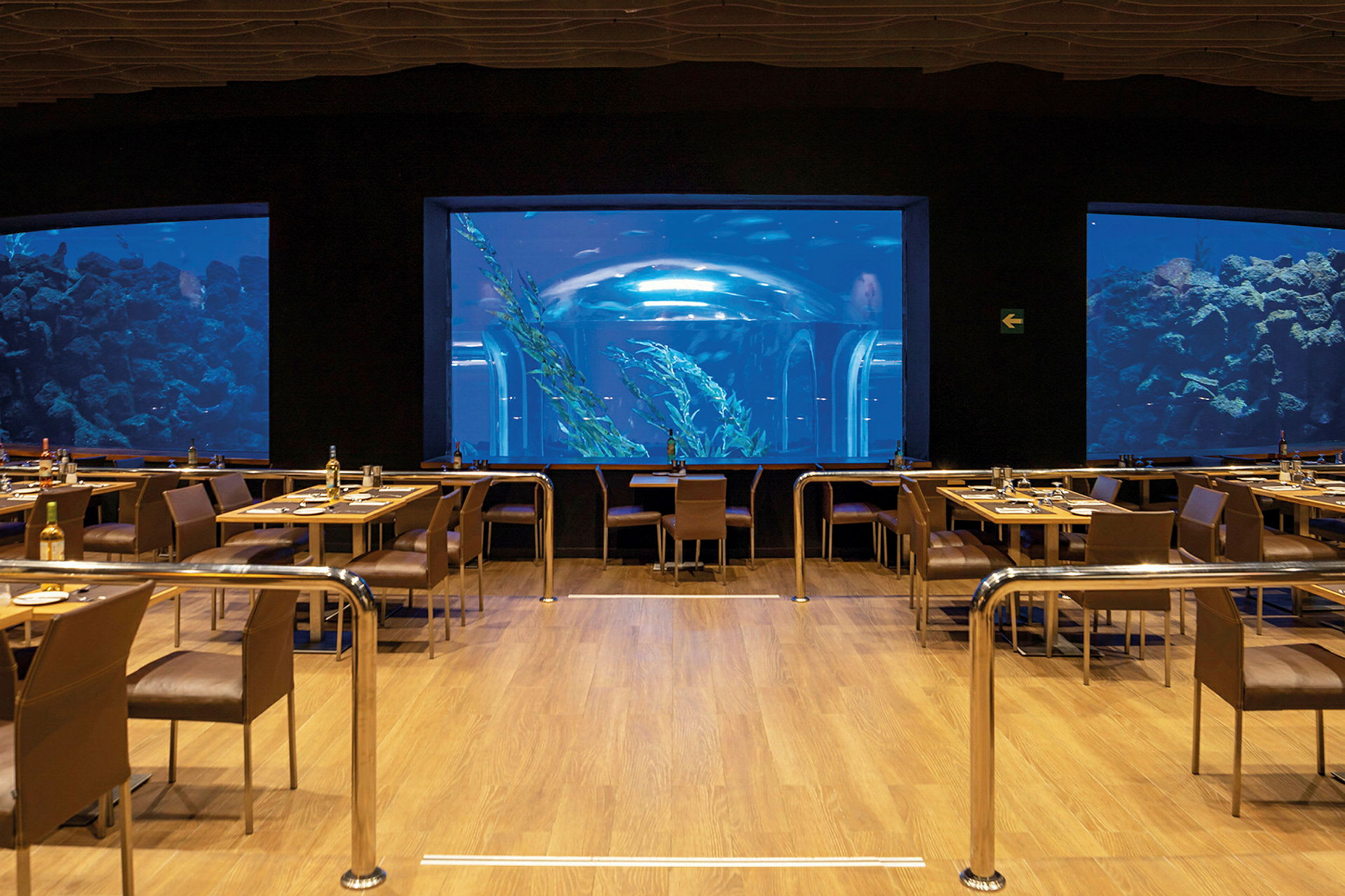 En restaurant med utsikt over et stort akvarium med fisker og undervannsmiljø. (AI-generert tekst)