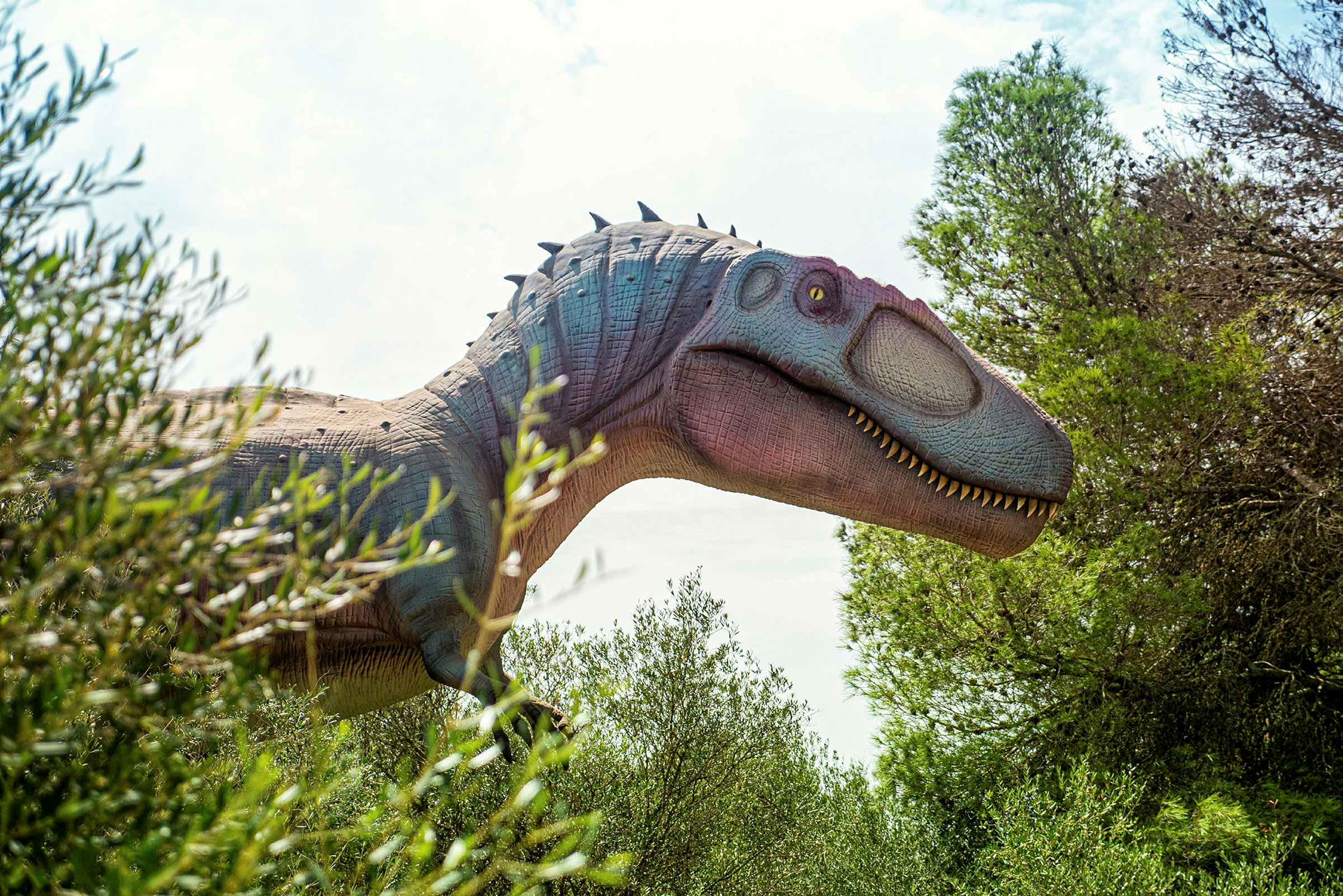 En replika av en dinosaur kan sees delvis blant vegetasjon og trær. (AI-generert tekst)