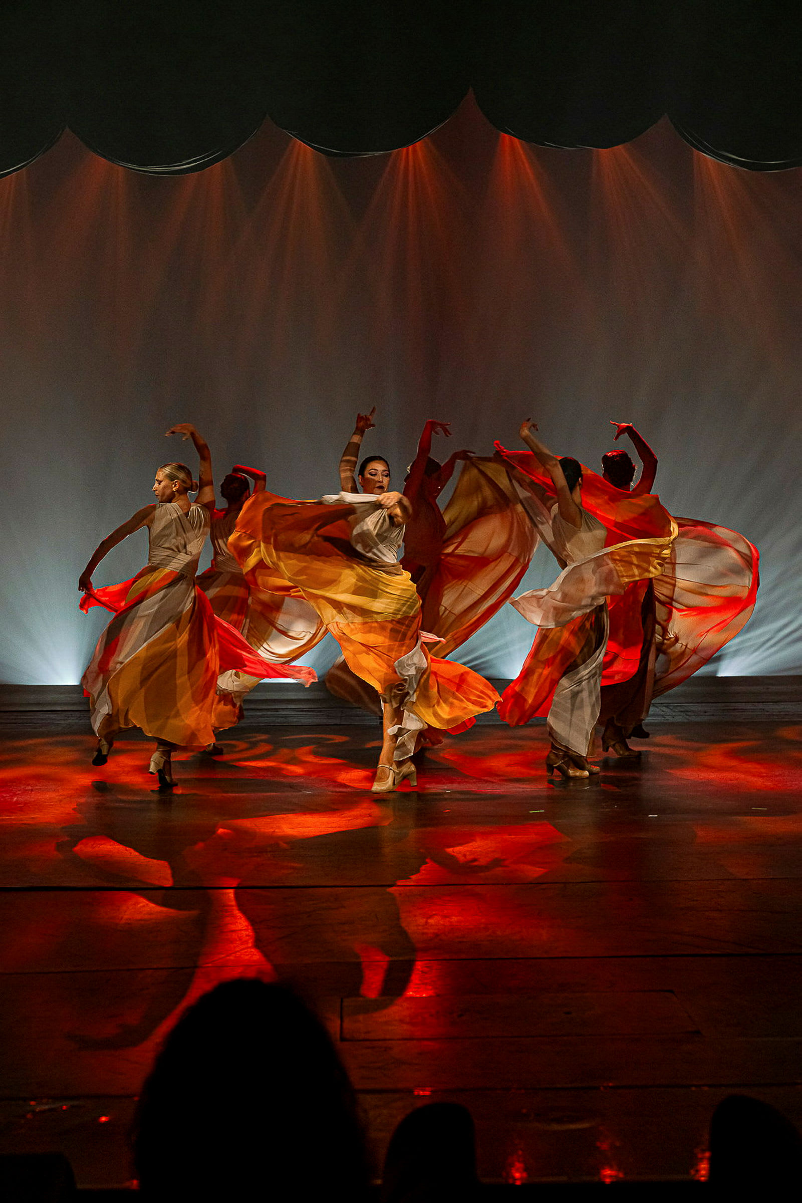 En gruppe dansere fremfører en koreografi på en scene med rødt og oransje lys. (AI-generert tekst)