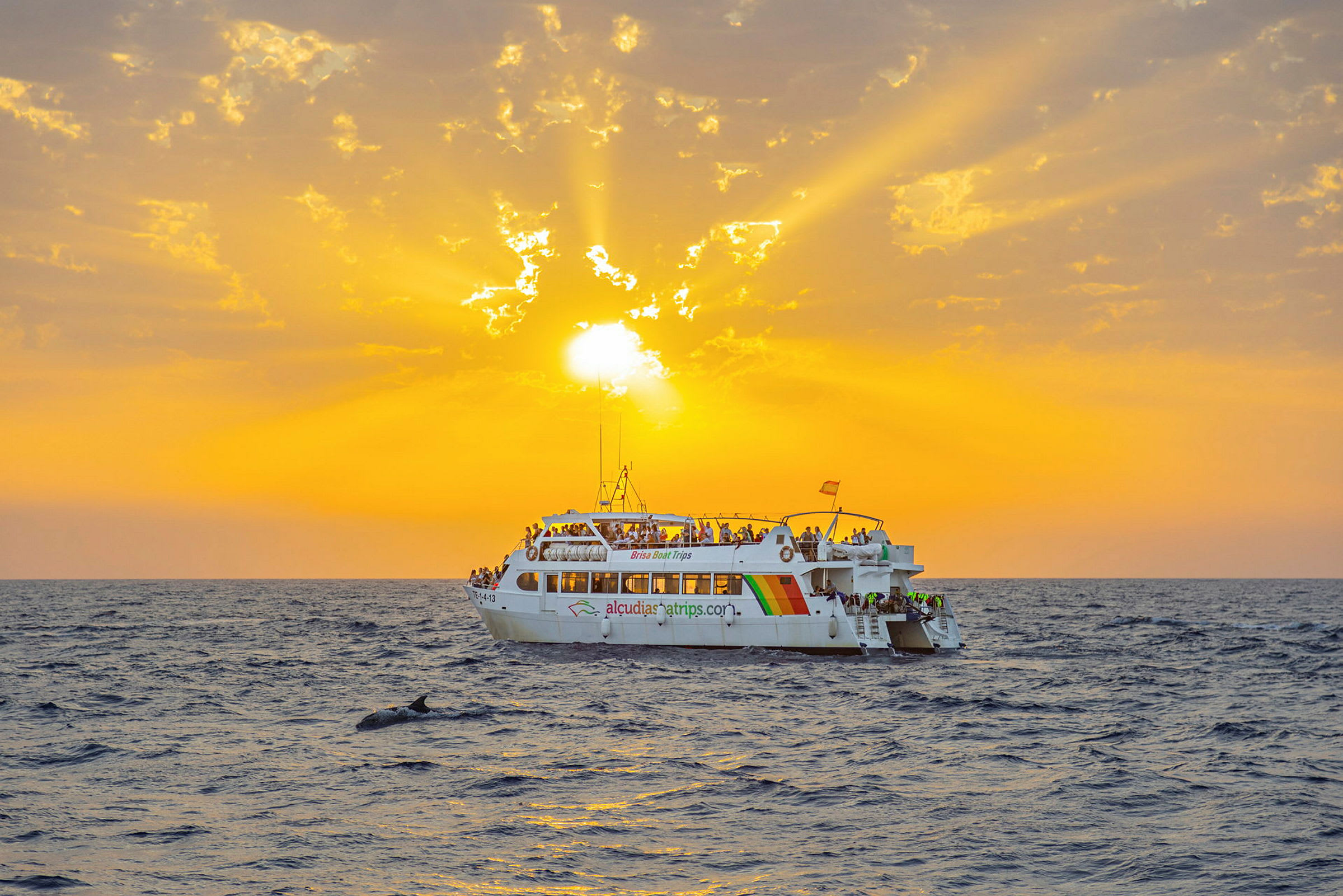 En hvit båt med mennesker på dekket flyter på havet under en oransje solnedgang. (AI-generert tekst)