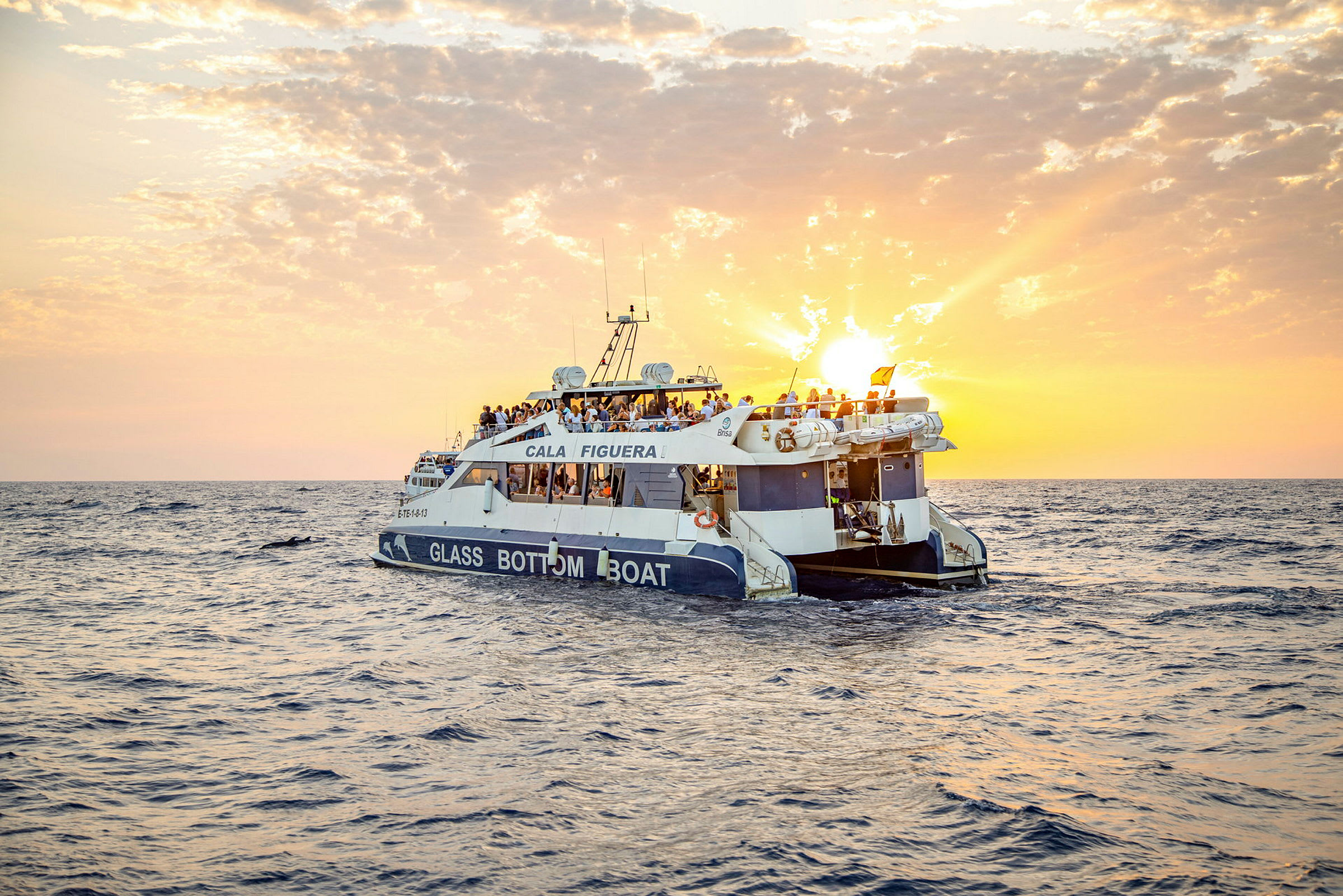 En glassbunnbåt med mennesker om bord seiler på havet under en solnedgang. (AI-generert tekst)