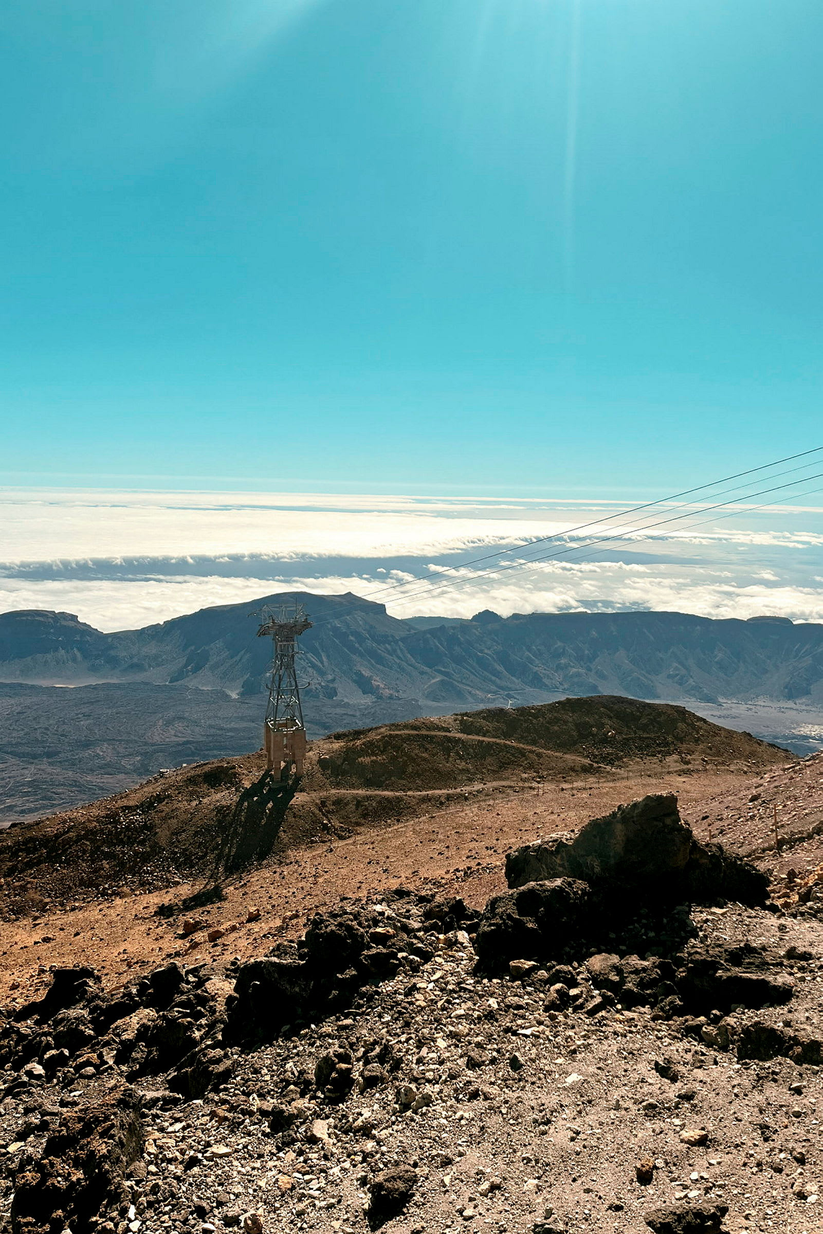 Et fjellandskap med en taubanelinje og stolpe, under en klar blå himmel. (AI-generert tekst)