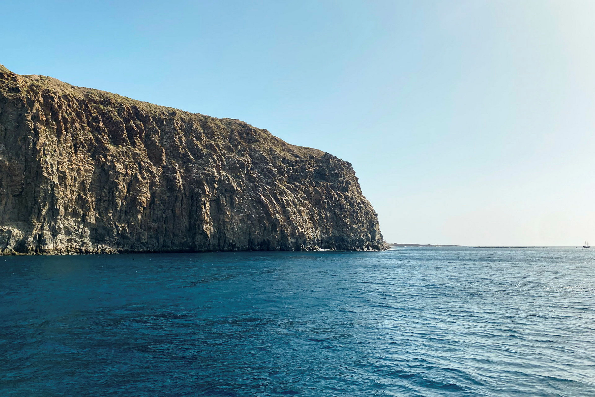 En høy klippe ved havet under klar blå himmel. (AI-generert tekst)