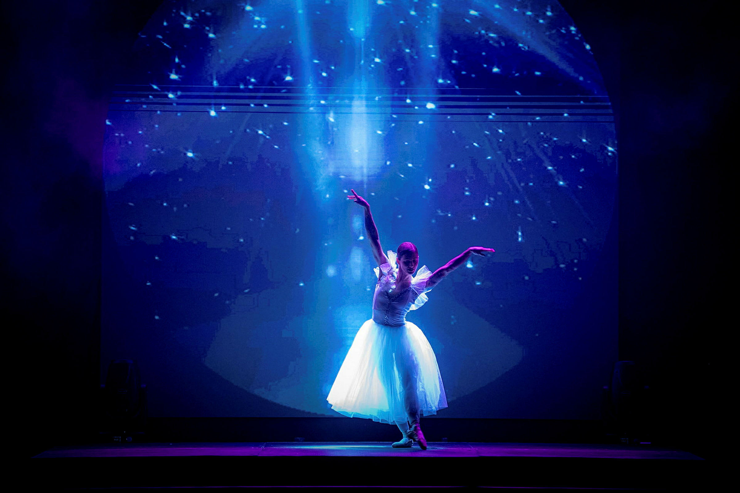 En ballettdanser i hvit kjole poserer på en scene med en stjernefyllt bakgrunn. (AI-generert tekst)