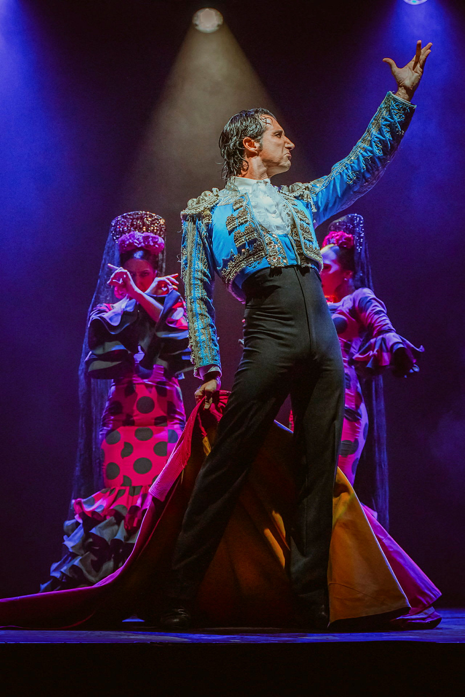 En flamencodanser iført fargerike klær poserer på en scene med to bakgrunnsdanserne i tradisjonelle antrekk. (AI-generert tekst)