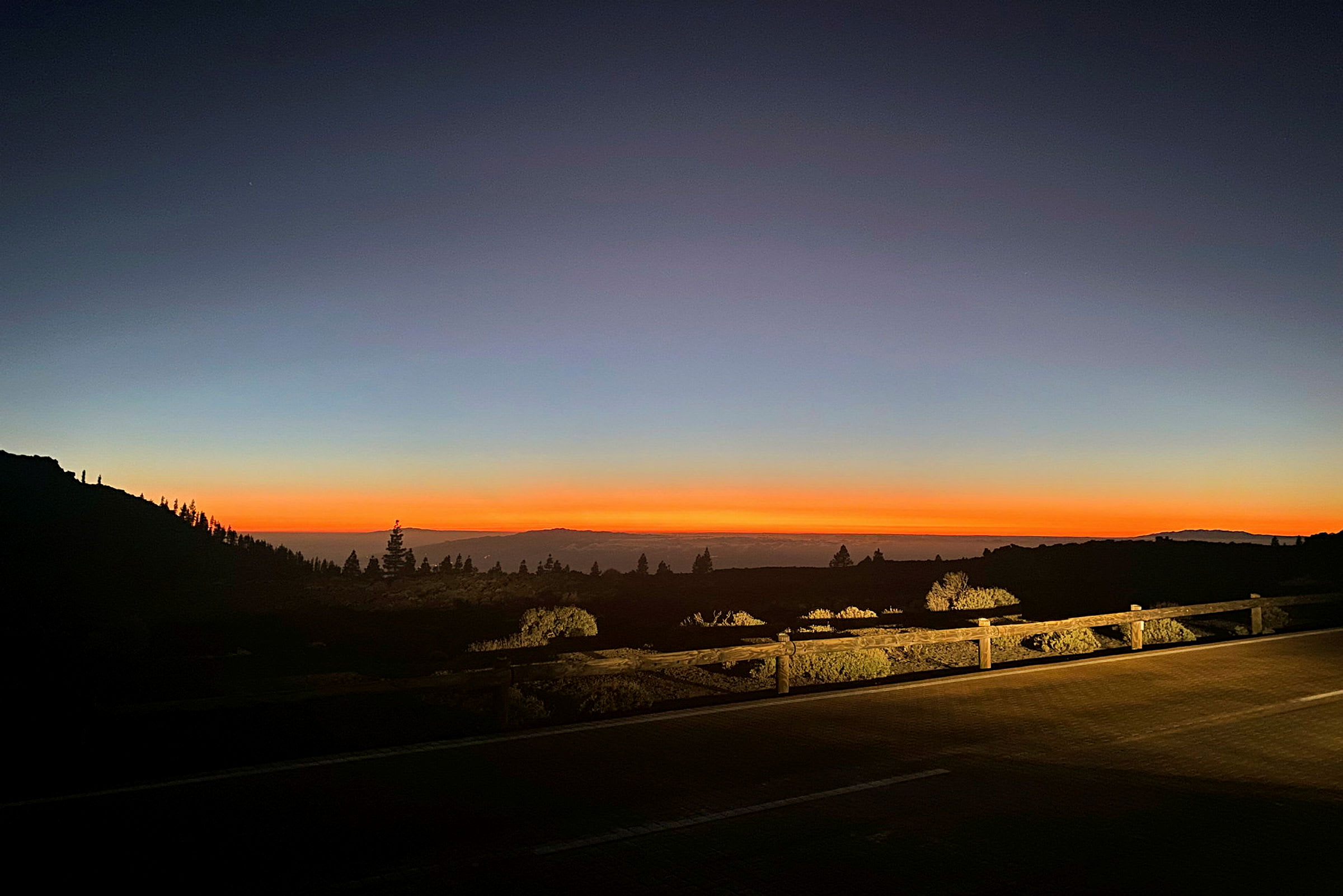 En solnedgang over et landskap med vegetasjon og en vei i forgrunnen. (AI-generert tekst)