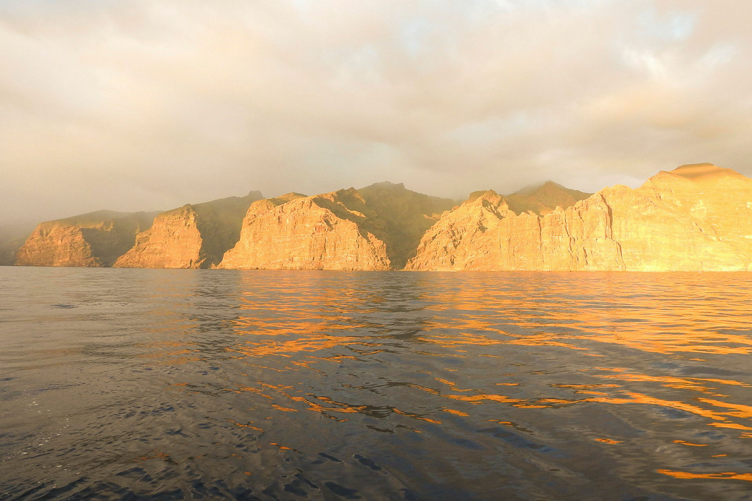 Solbelyste klipper ved havet under overskyet himmel. (AI-generert tekst)