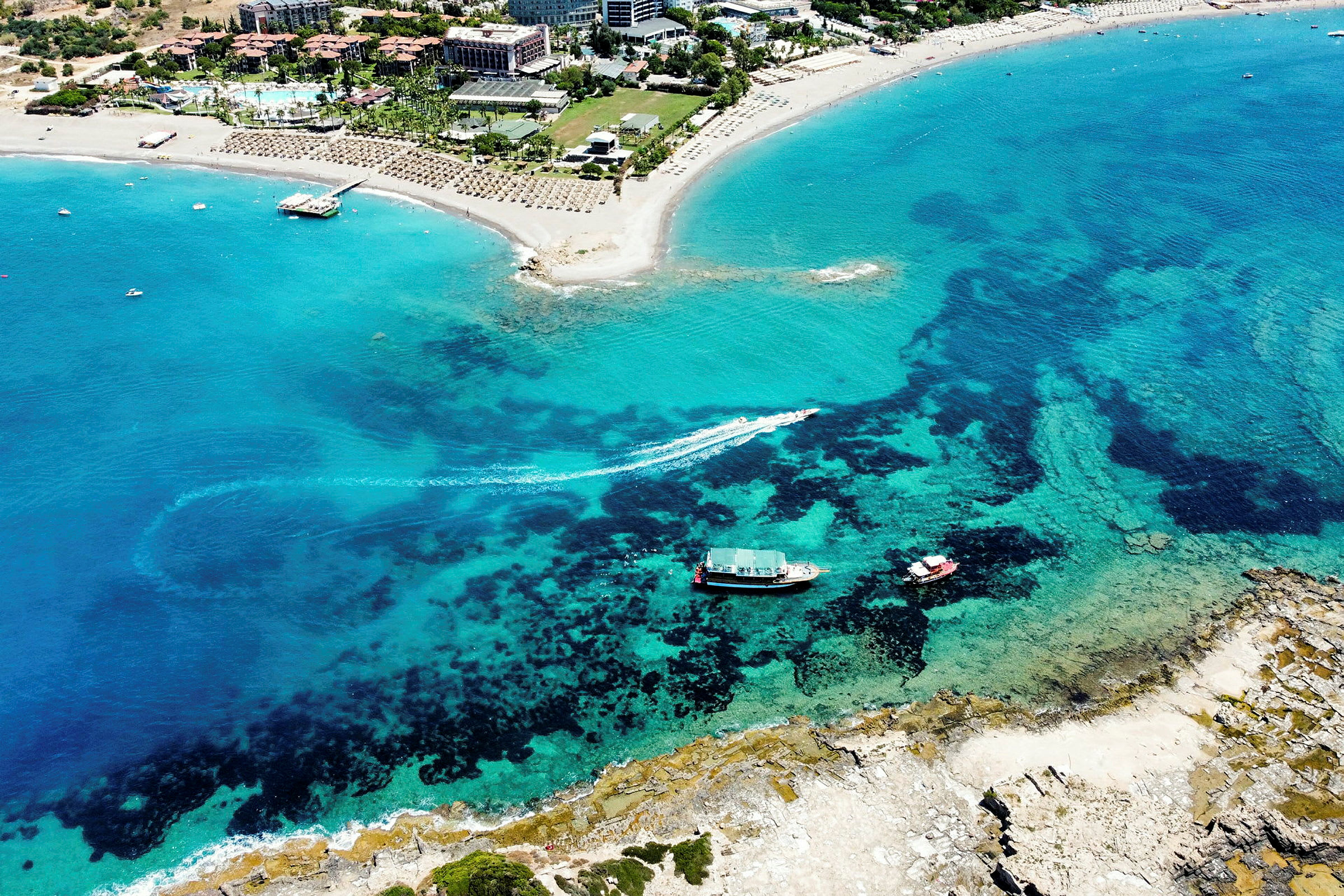 Luftfoto av en sandstrand ved et turistområde med klart blått vann. (AI-generert tekst)