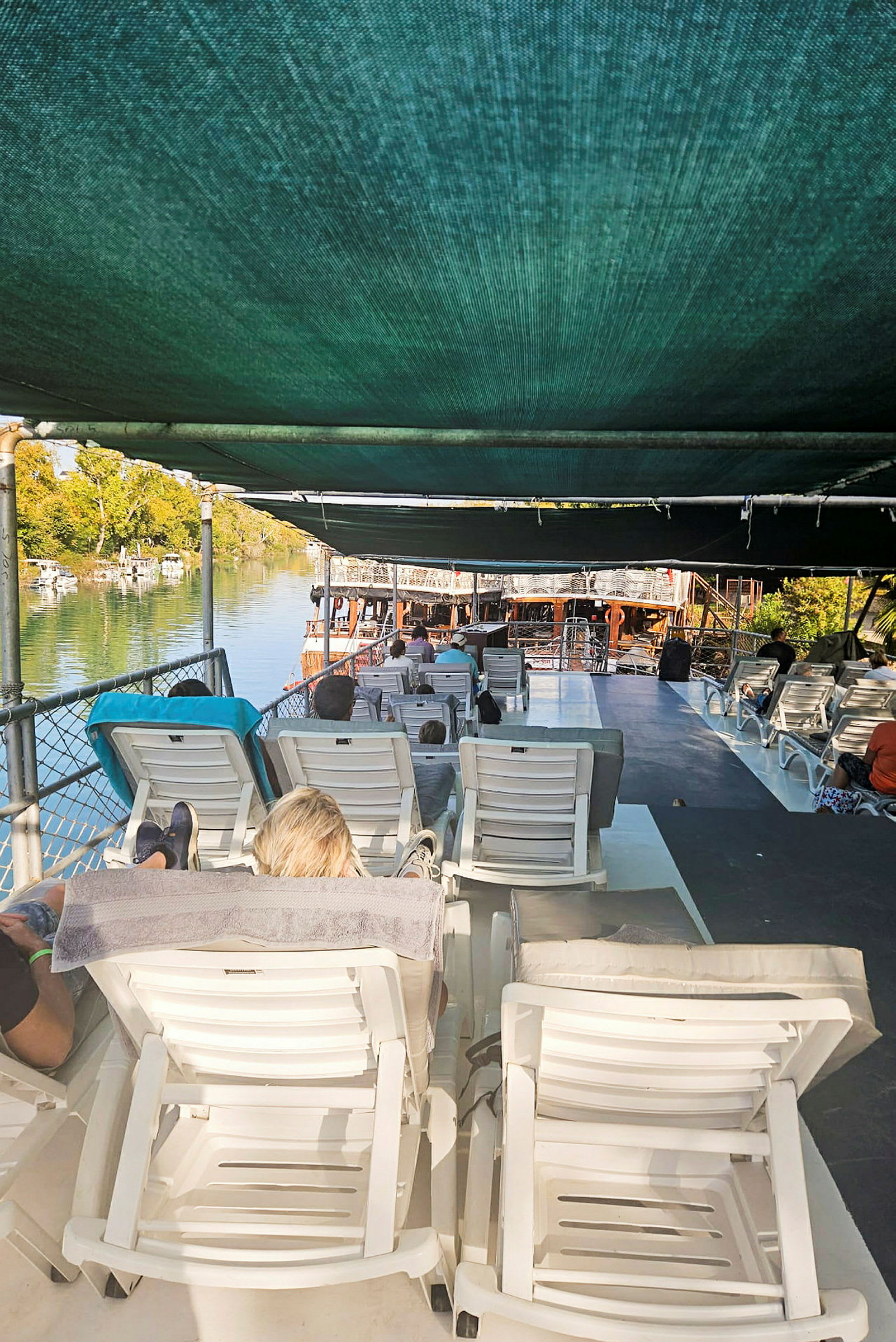 Personer ligger på solsenger under et skyggende tak på en båt ved vannet. (AI-generert tekst)