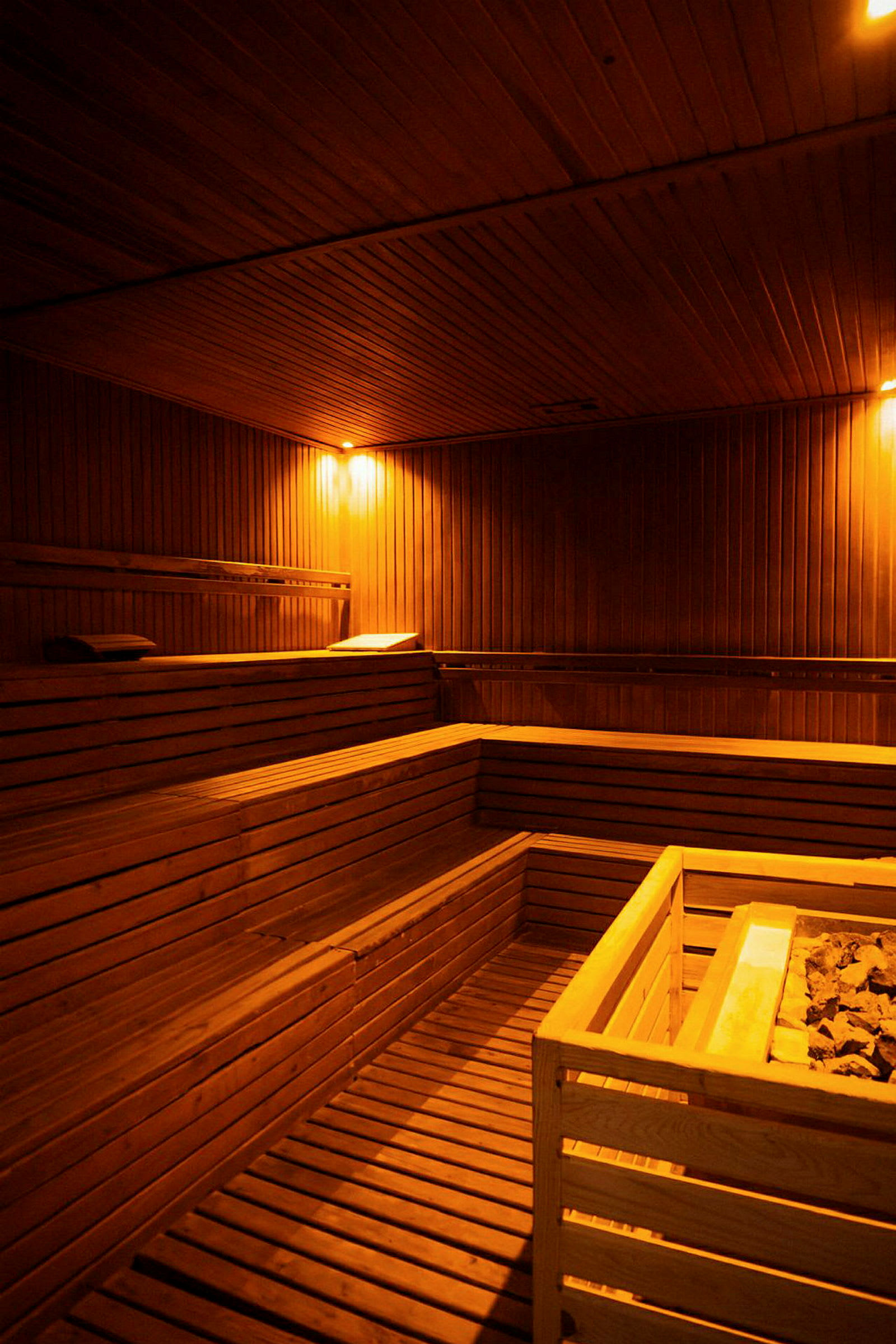 Et rom laget av tre med sauna benker og en sentralt plassert saunaovn. (AI-generert tekst)