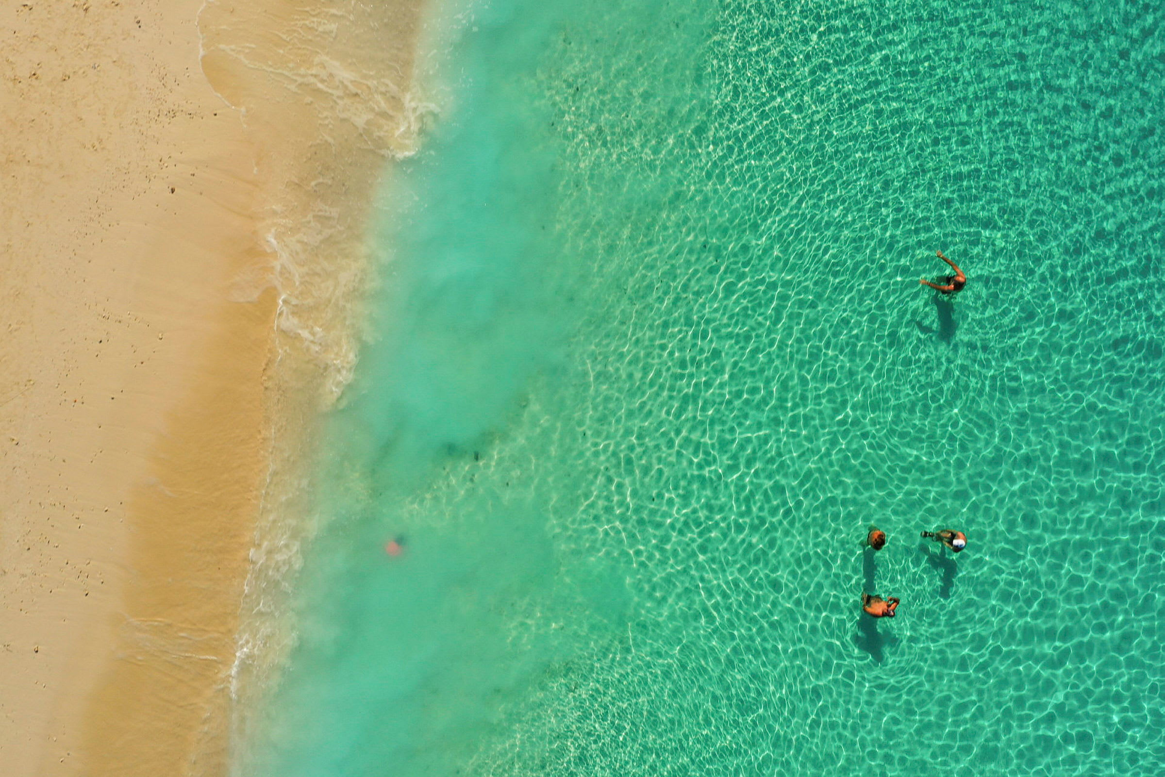Dronefoto av personer som svømmer i sjøen nær en sandstrand. (AI-generert tekst)
